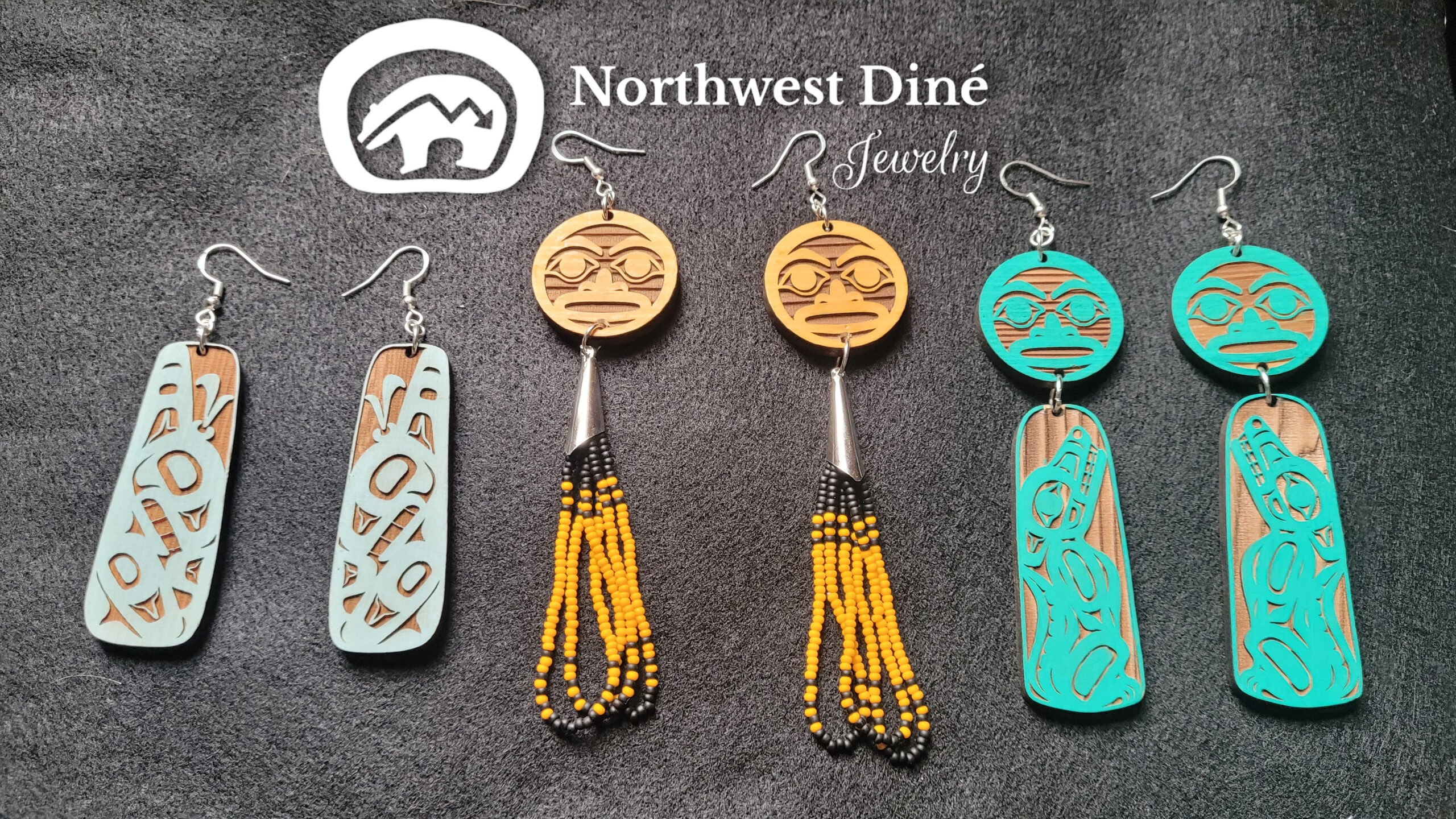 Jewelry display showing a pair of earrings from each collection from Northwest Diné Jewelry, Orca, Moon, and Wolf earrings featuring Tlingit formline designs by Native artist Wéidaaká Yóodóohaa